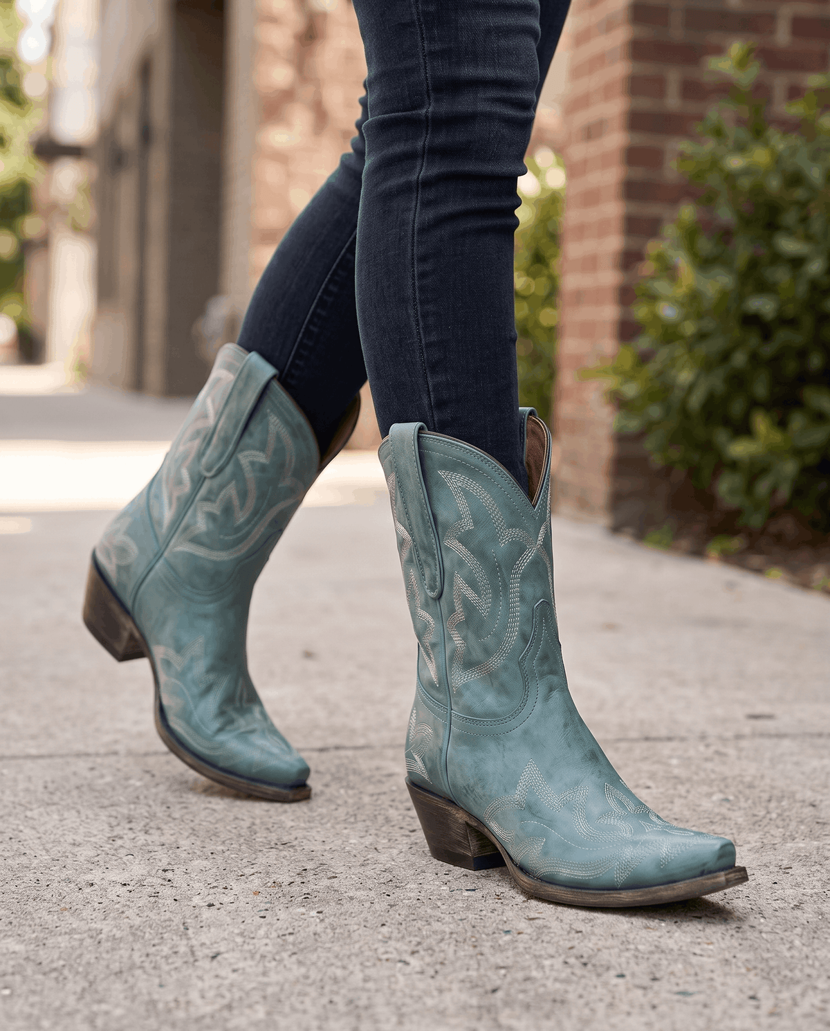 Teal western boots worn walking on a city sidewalk with dark skinny jeans
