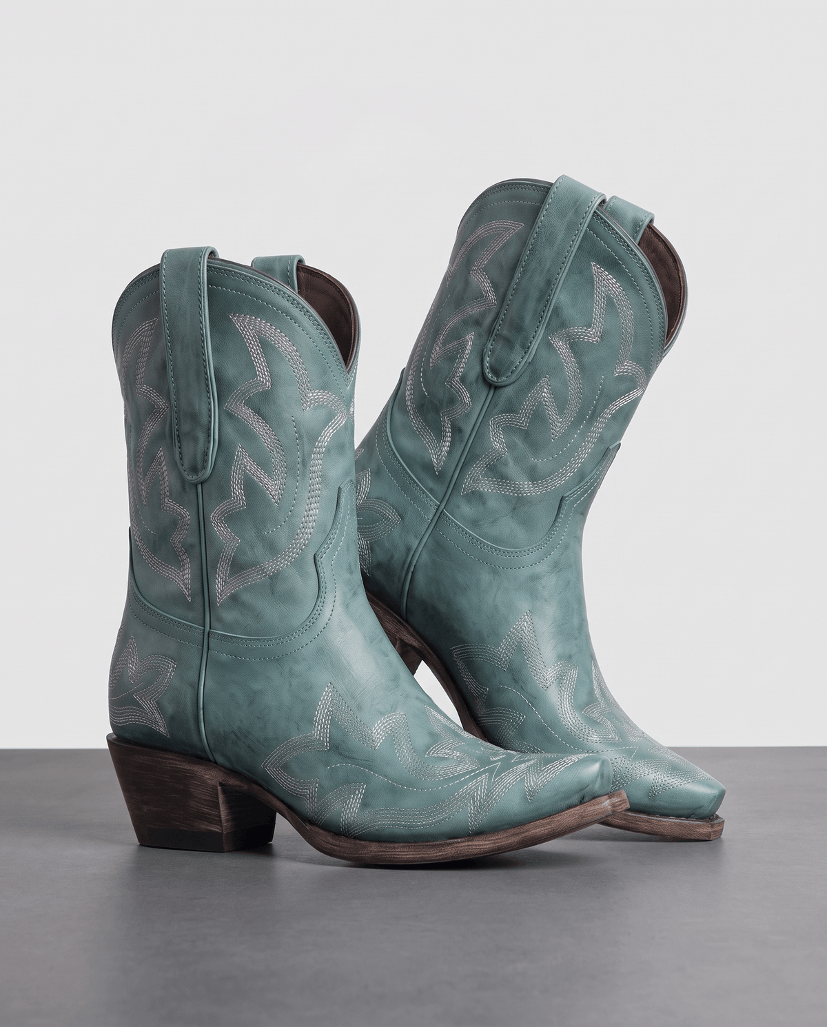 Pair of teal embroidered western boots on a grey studio floor