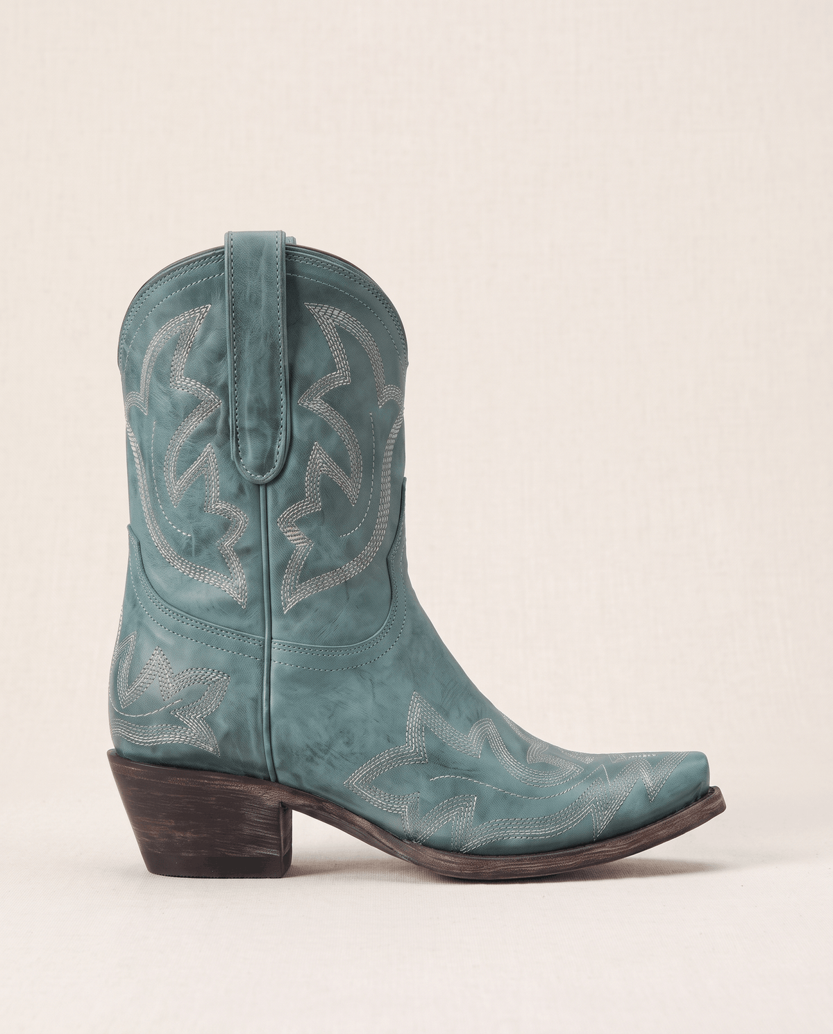 Single teal boot in side profile showing the snip toe and stacked heel