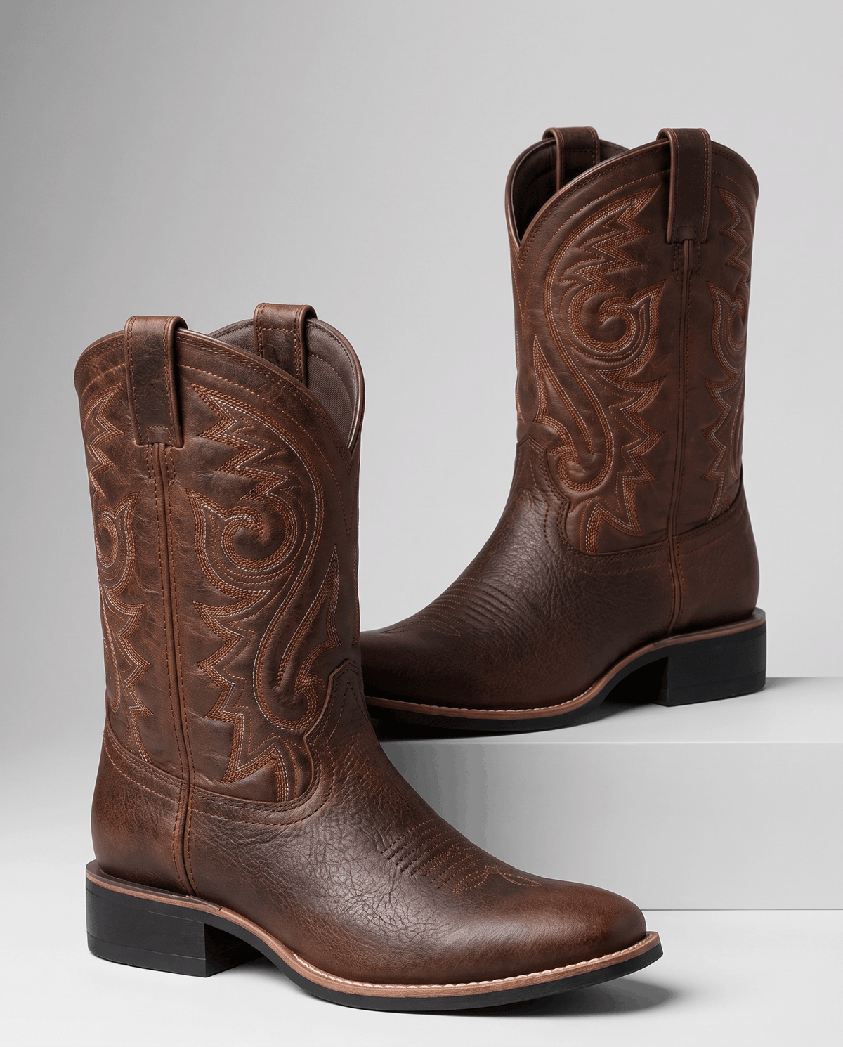 Brown embroidered western boots displayed on white steps against a grey backdrop
