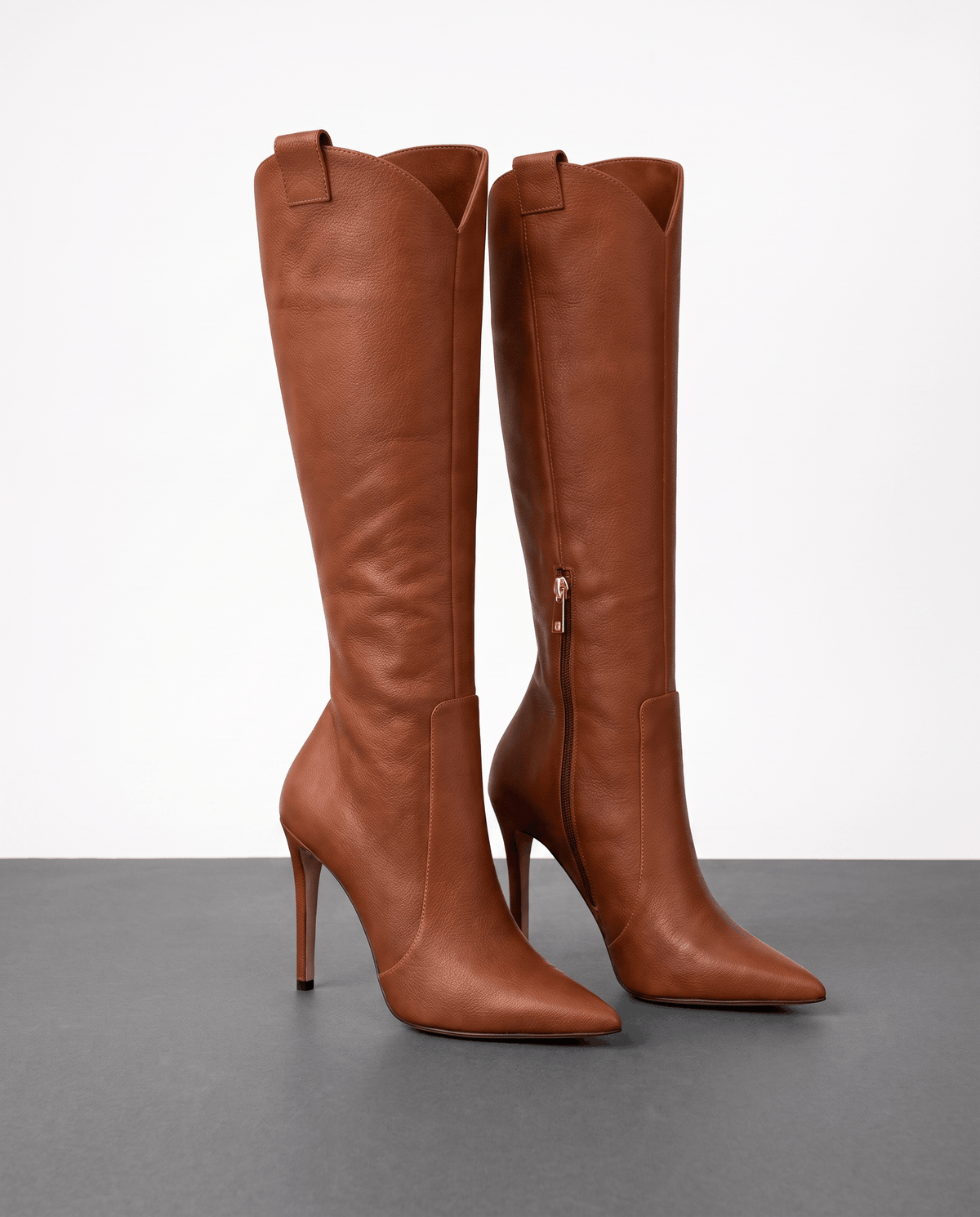 Brown smooth-grain knee-high boots with a pointed toe, slim stiletto heel, close-cut shaft, side zip, and collar pull tab.