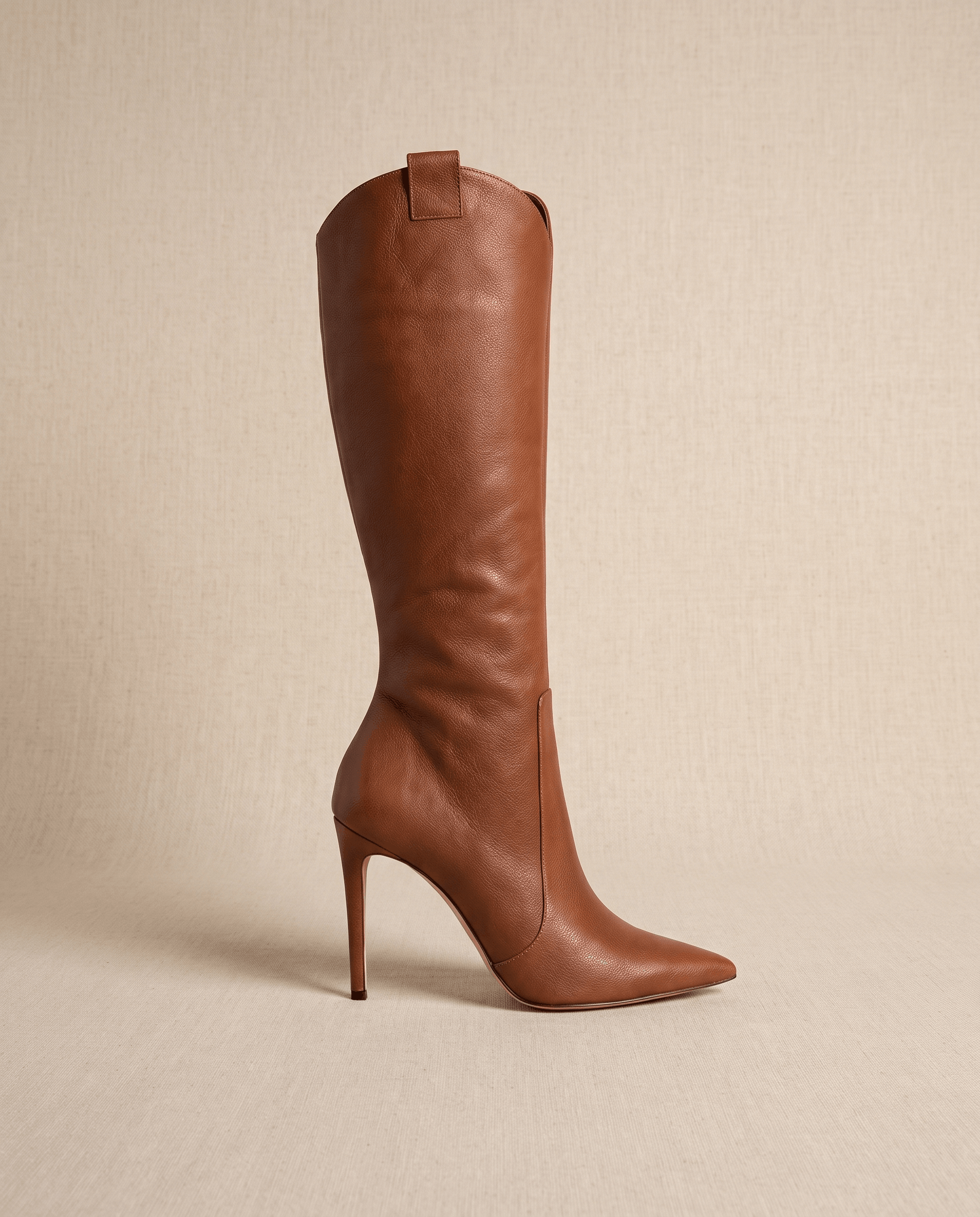 Brown smooth-grain knee-high boots with a pointed toe, slim stiletto heel, close-cut shaft, and collar pull tab.