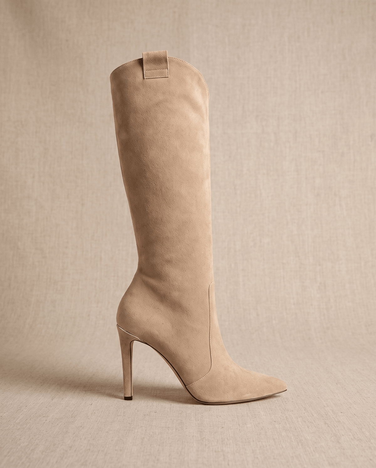 Beige suede knee-high boots with a pointed toe, slim stiletto heel, close-cut shaft, and a collar pull tab.
