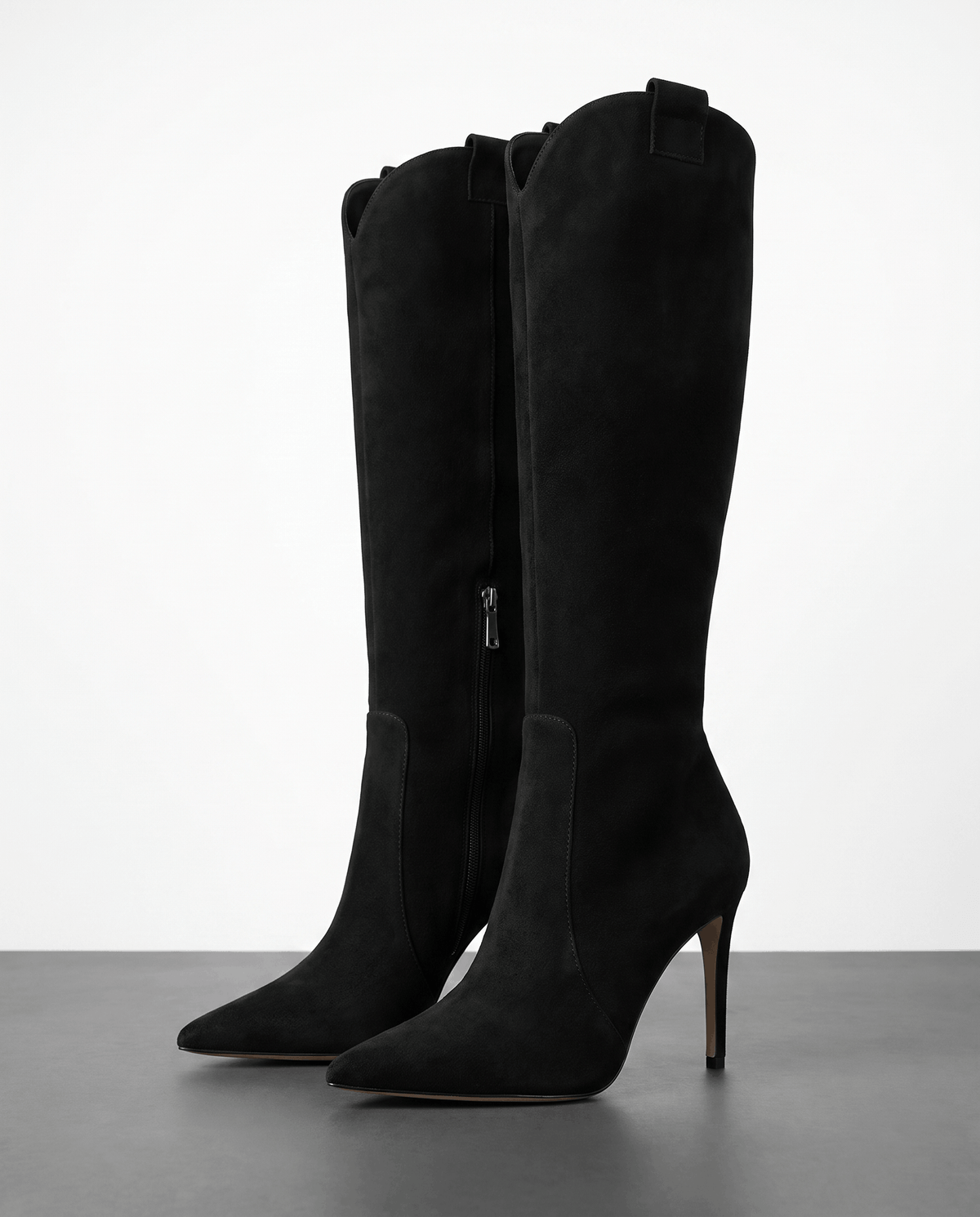 Black suede knee-high boots with a pointed toe, slim stiletto heel, close-cut shaft, side zip, and collar pull tab.