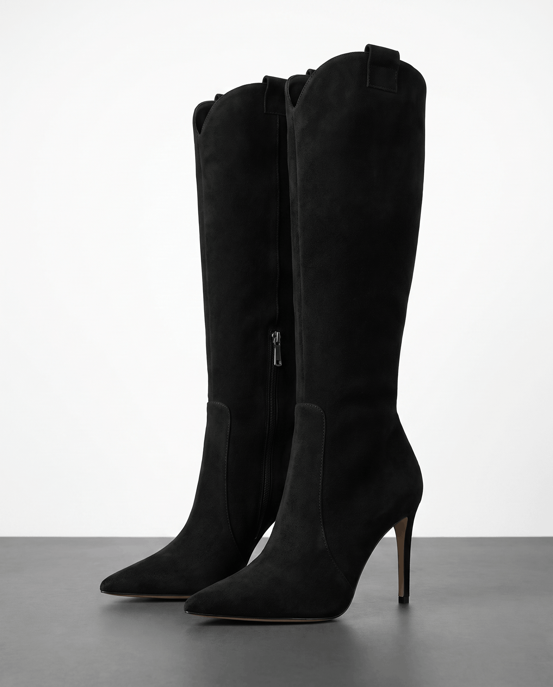 Black suede knee-high boots with a pointed toe, slim stiletto heel, close-cut shaft, side zip, and collar pull tab.