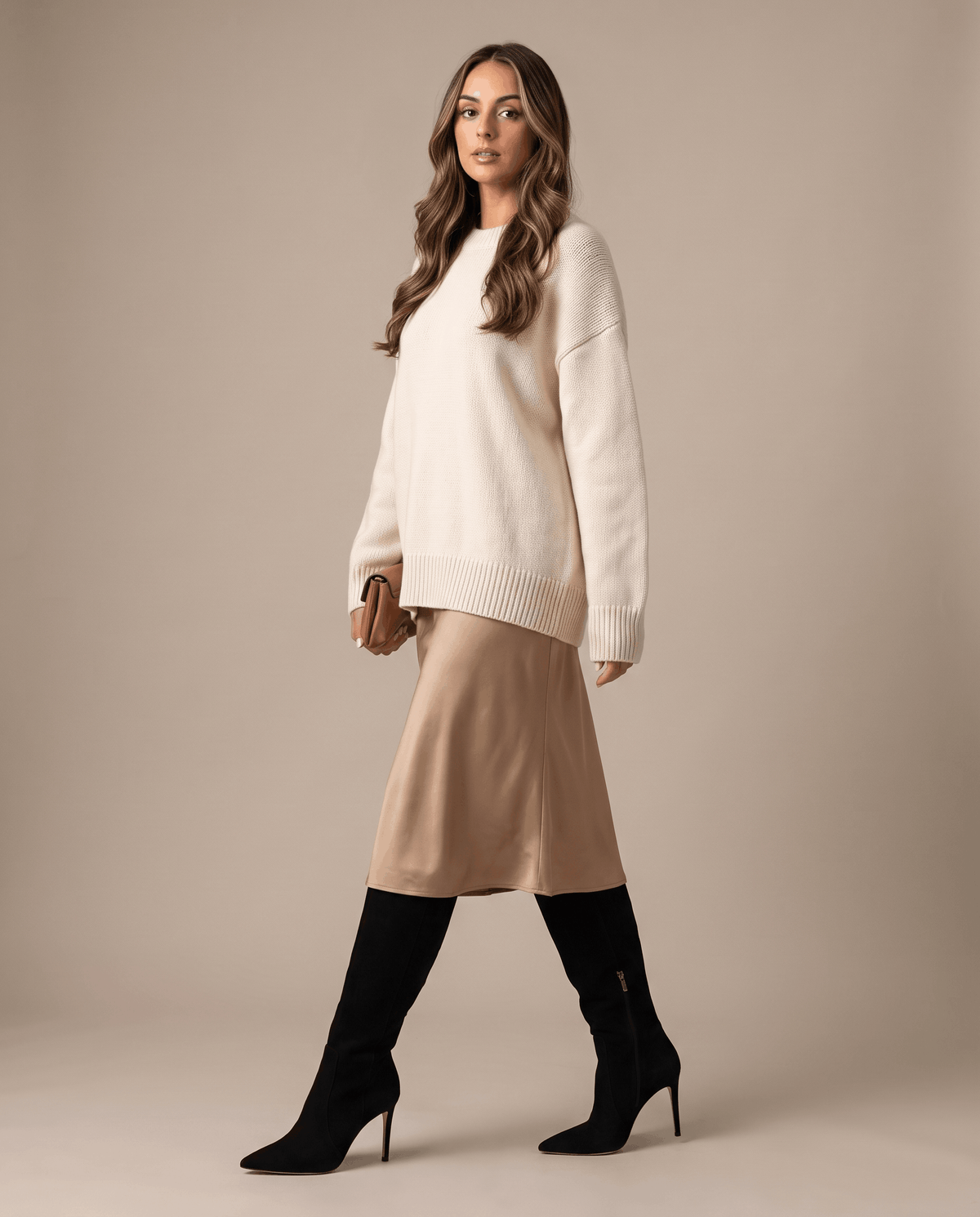 Black knee-high stiletto boots with a pointed toe and close-cut shaft, styled with a midi skirt and cream sweater.