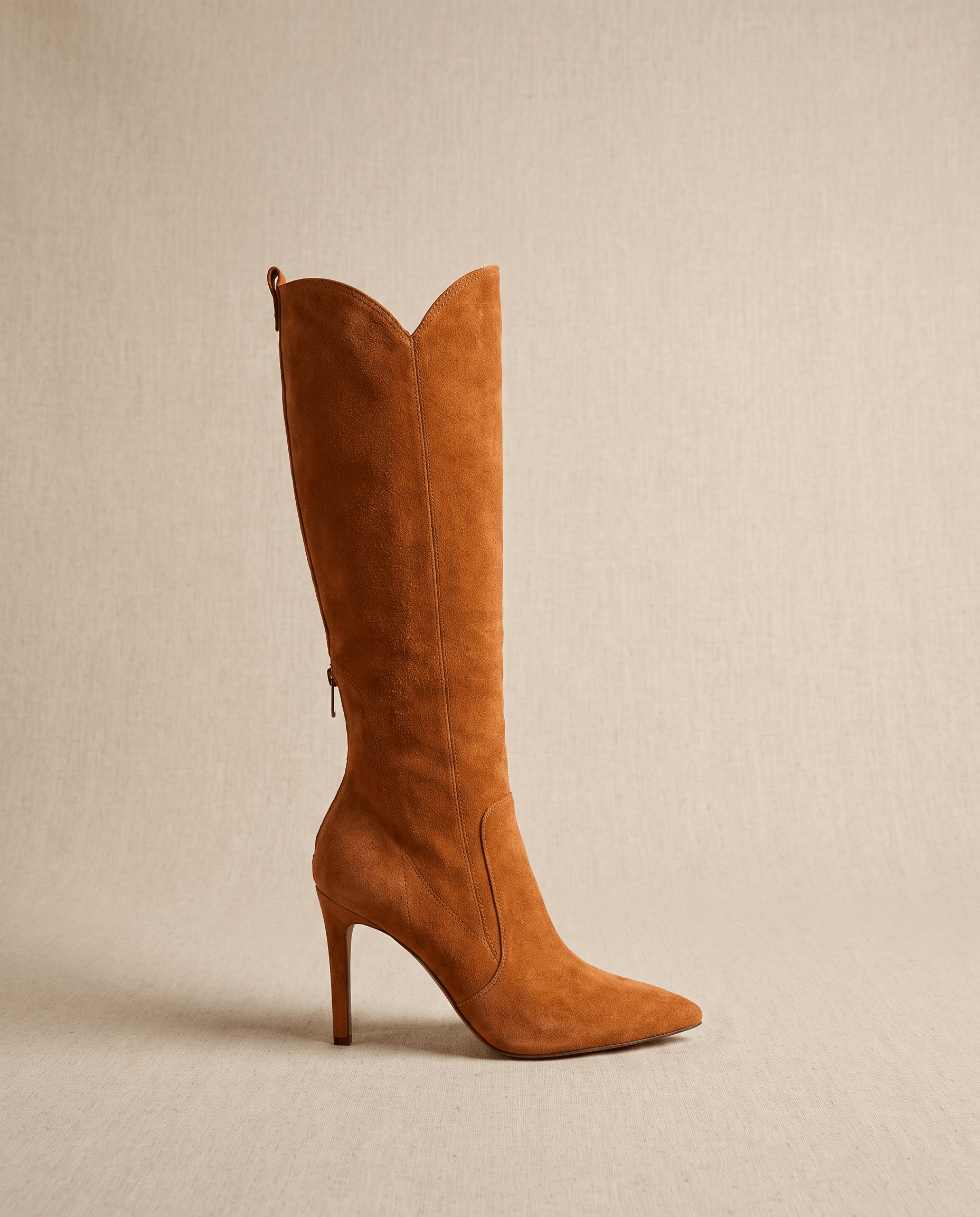 Camel suede knee-high boots featuring a pointed toe, slim stiletto heel, close-cut shaft, and a collar pull tab.