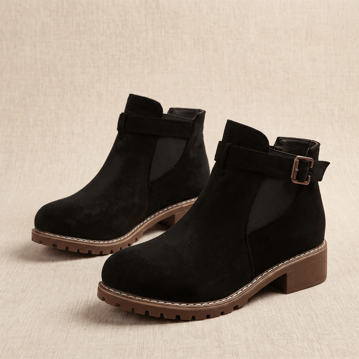 Pair of black suede ankle boots with buckle accents on a neutral background.