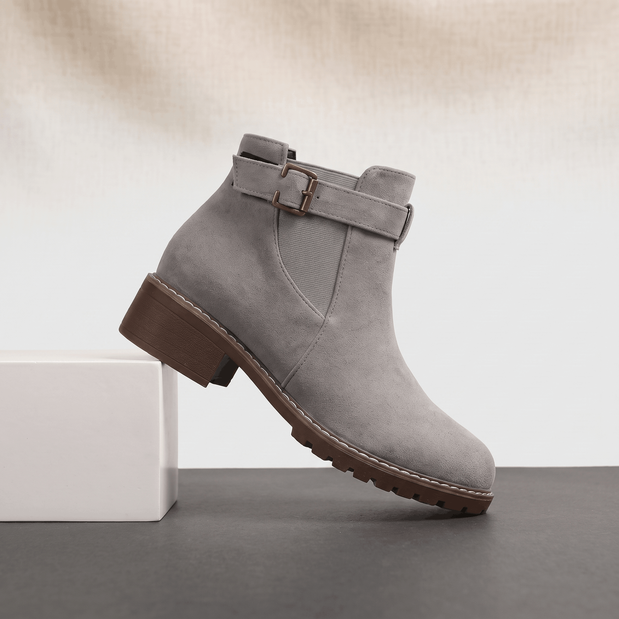 Light gray suede ankle boot with buckle detail and block heel displayed on a neutral background.