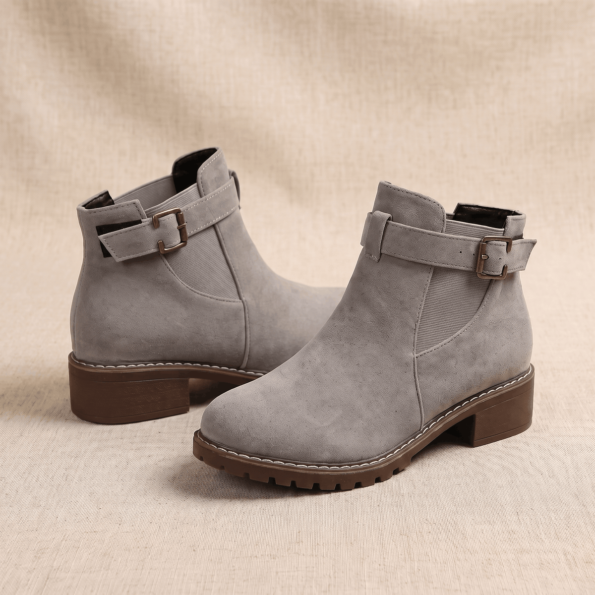 Pair of light gray suede ankle boots with buckle accents.