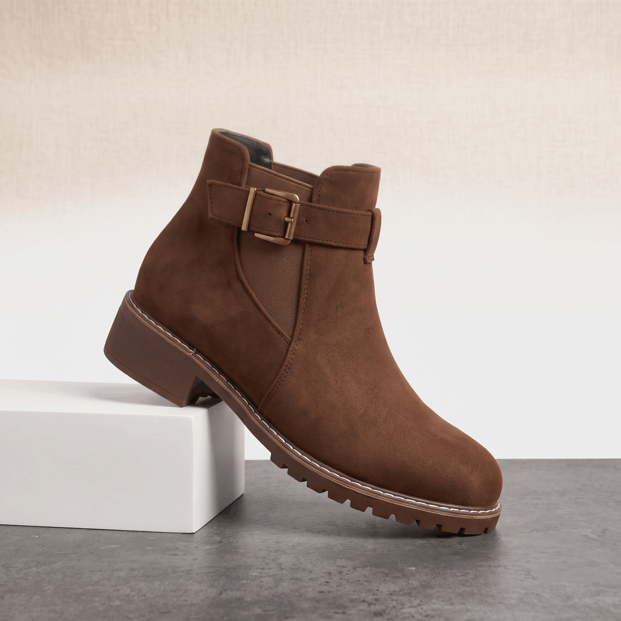 Dark brown suede ankle boot with a block heel displayed on a white pedestal.