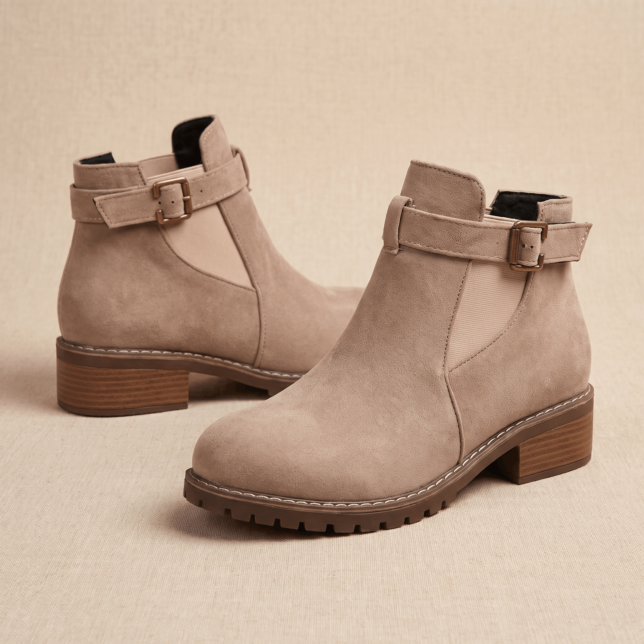 Pair of light beige suede ankle boots with buckle details on a neutral background.