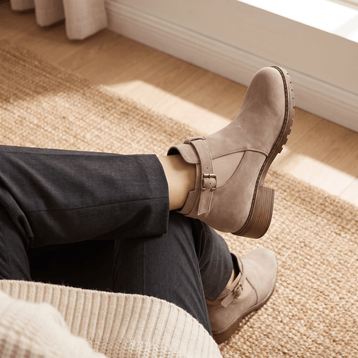 Close-up of light beige suede ankle boots worn while reclining on a sofa.