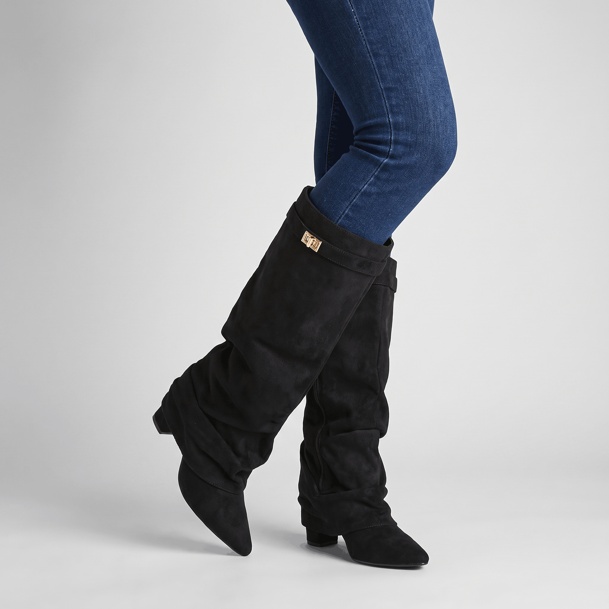 Woman wearing black suede fold-over knee-high boots with blue jeans.