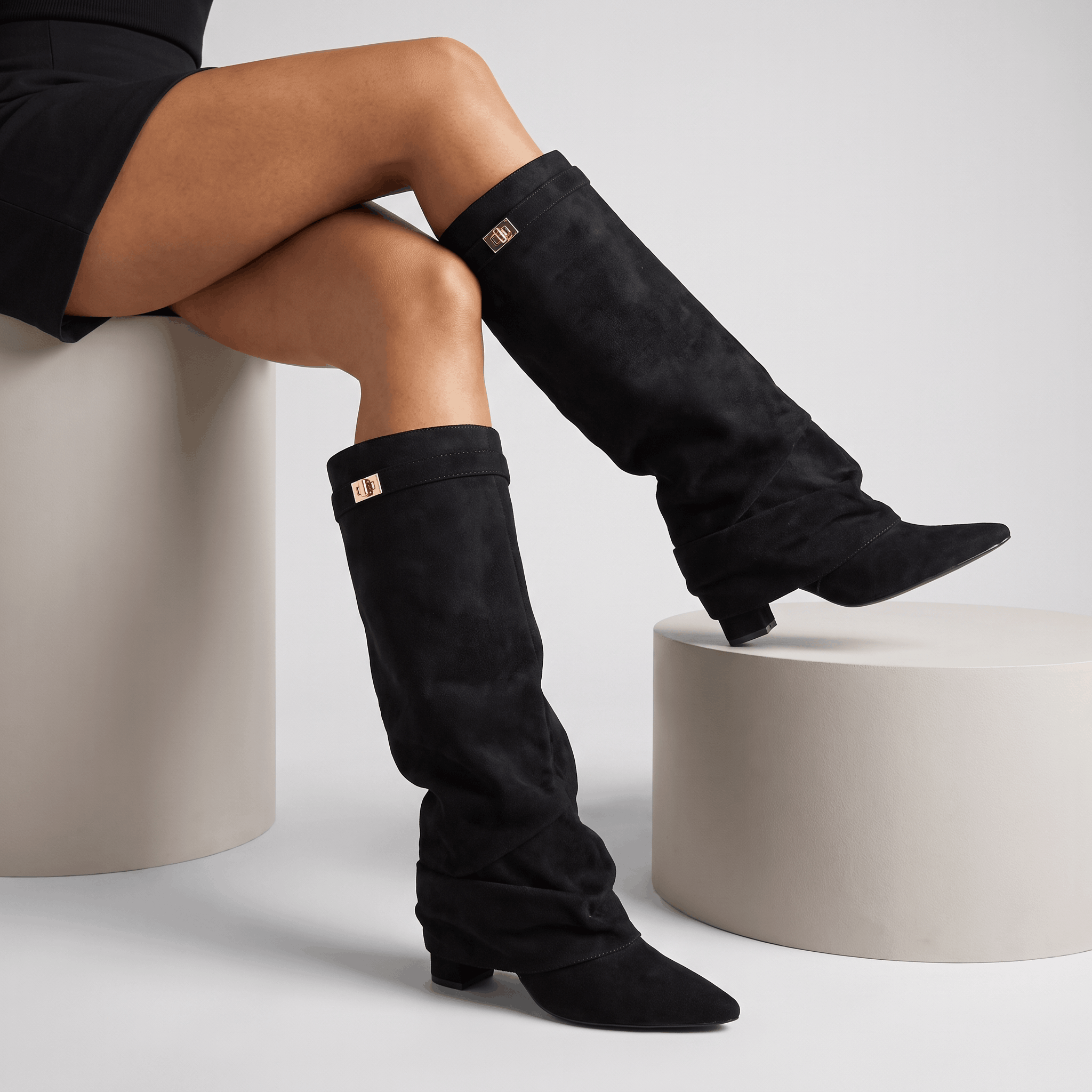 Woman seated wearing black suede fold-over knee-high boots with a full side zip.