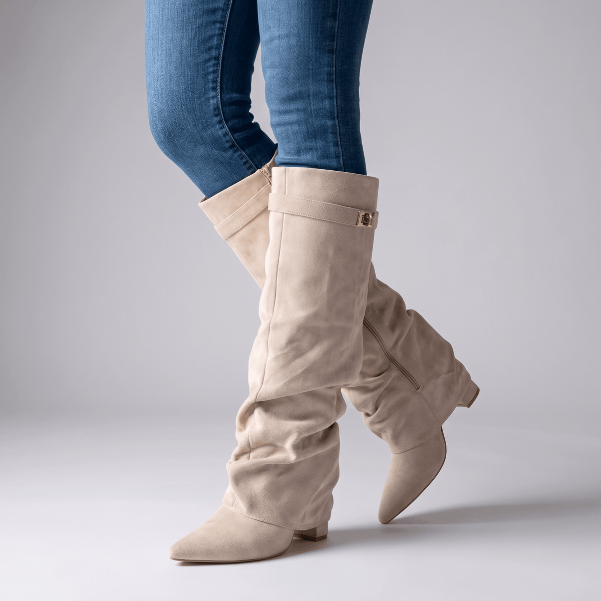 Woman wearing beige suede fold-over knee-high boots with blue jeans.