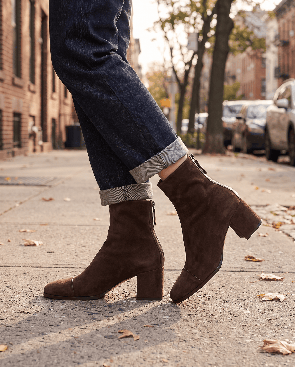 Brown suede block heel boots styled with cuffed dark jeans outdoors