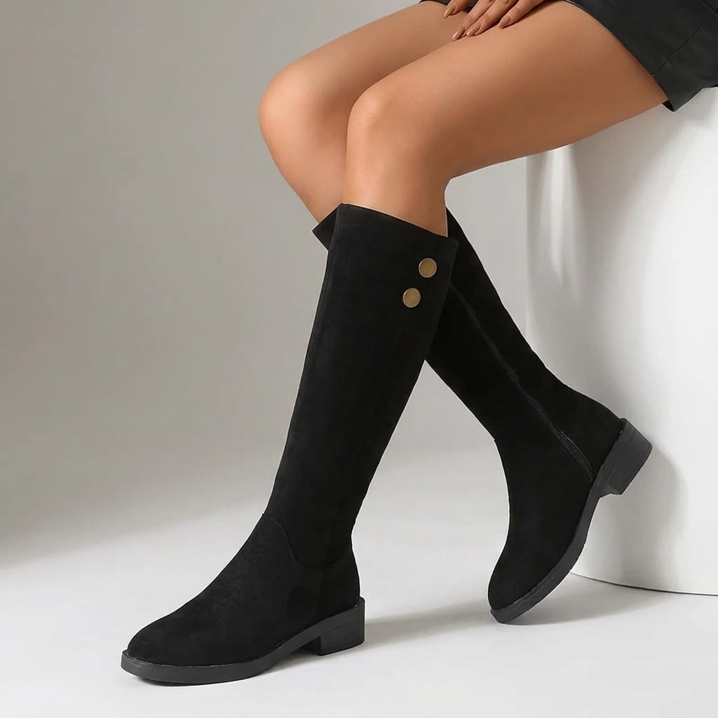 Woman wearing black knee-high boots with gold button details.