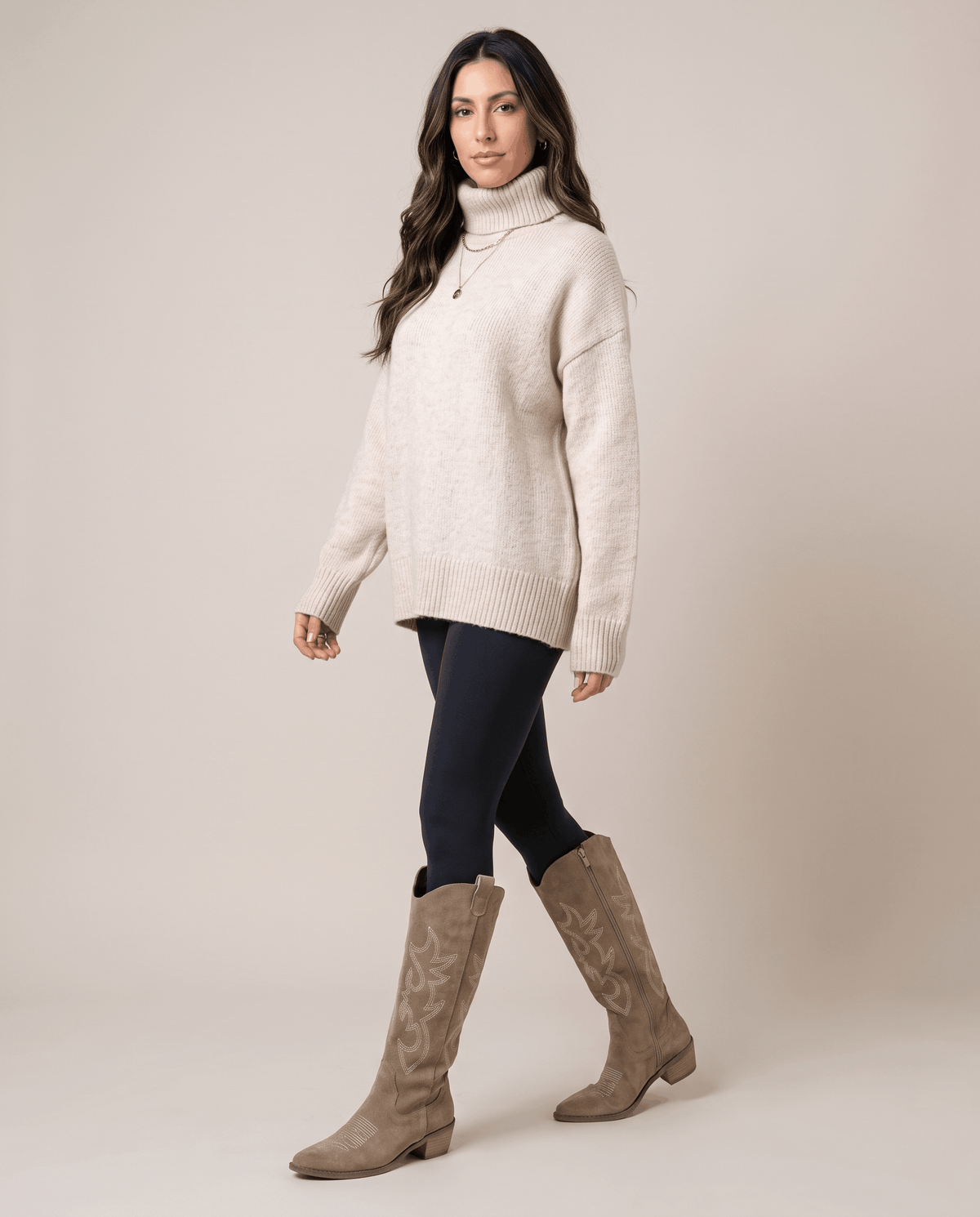 Woman in a cream turtleneck sweater and black leggings walking in beige boots