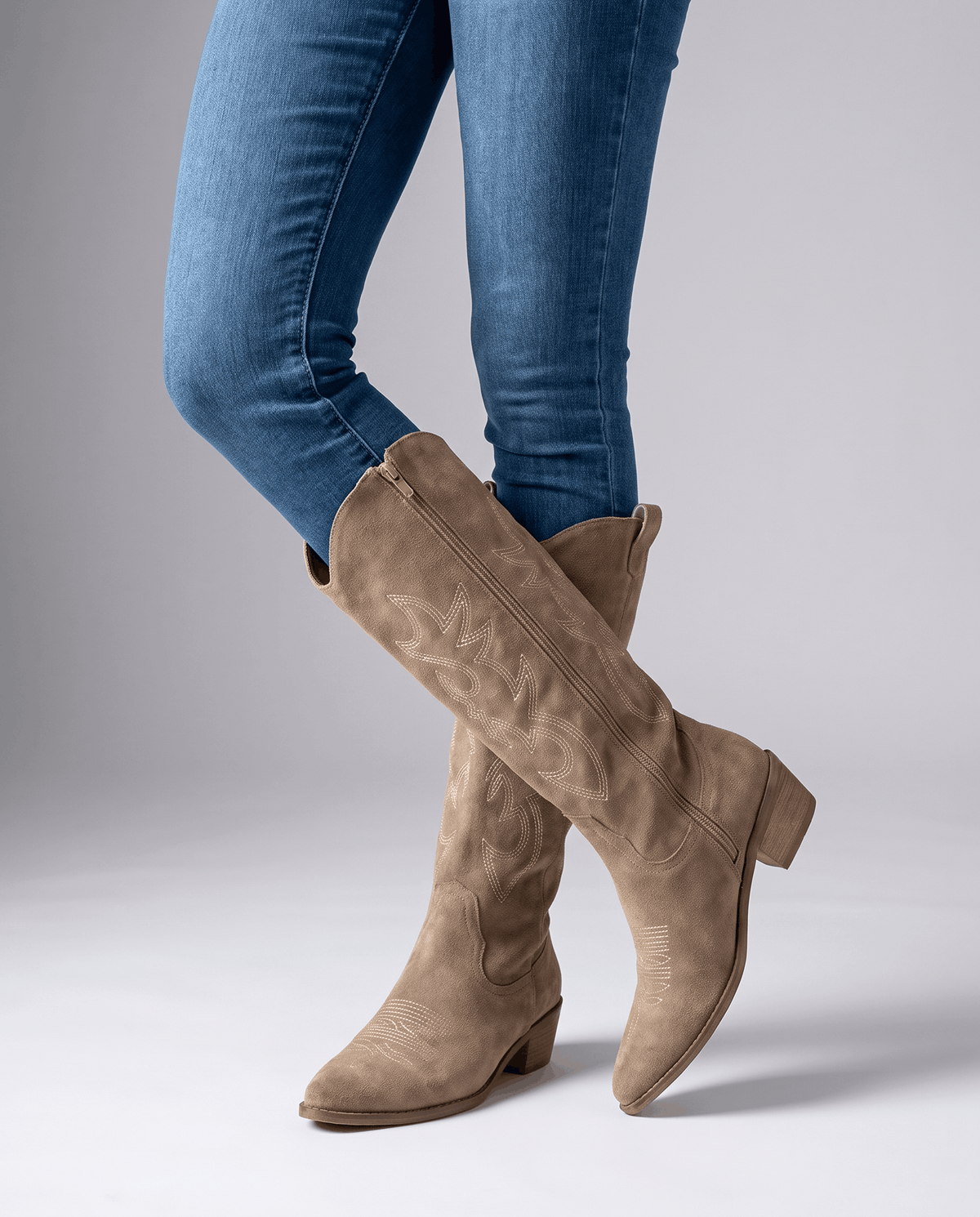 Model in blue skinny jeans tucked into beige embroidered boots, legs crossed