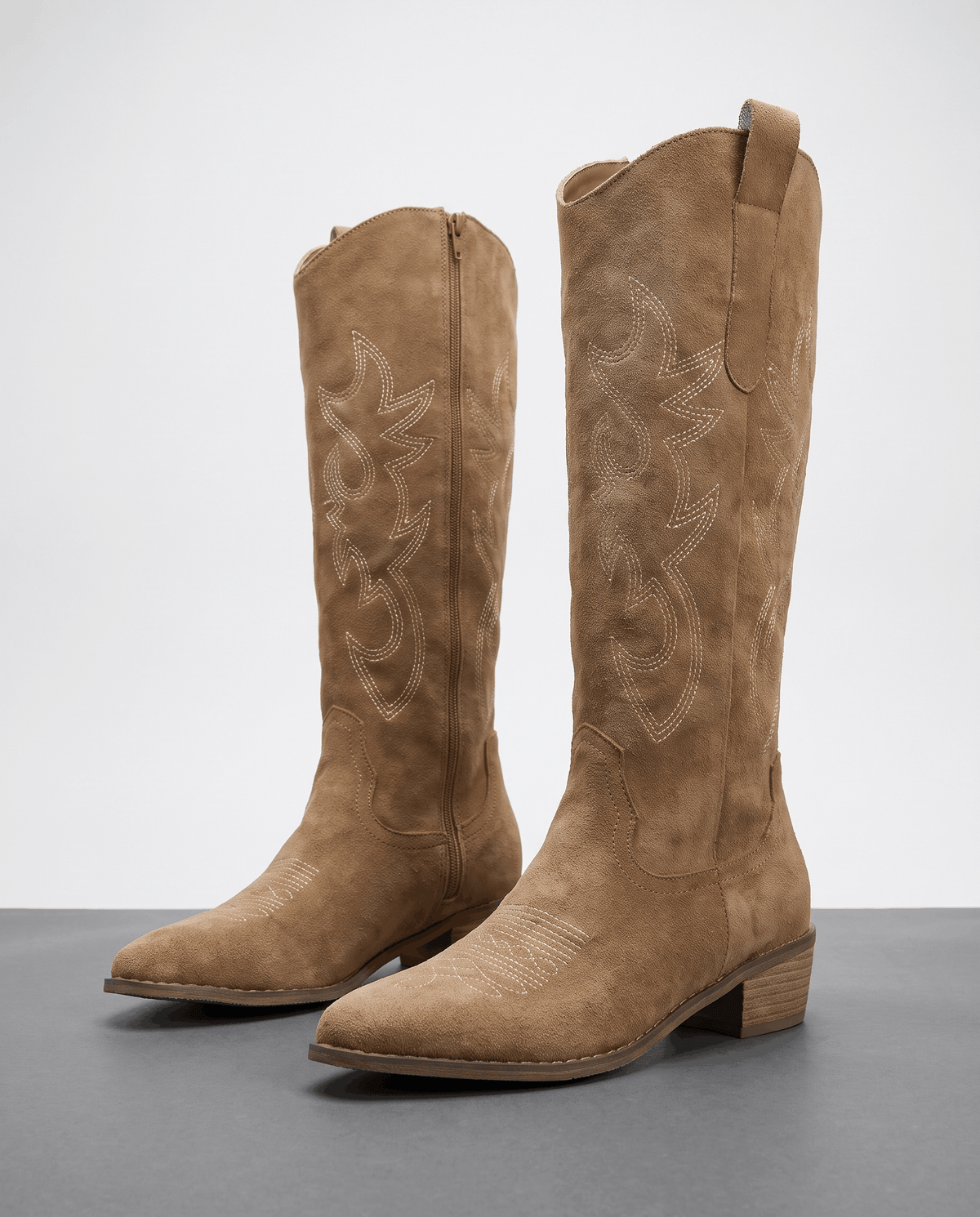 Pair of brown embroidered western boots with stacked heels on a grey studio floor