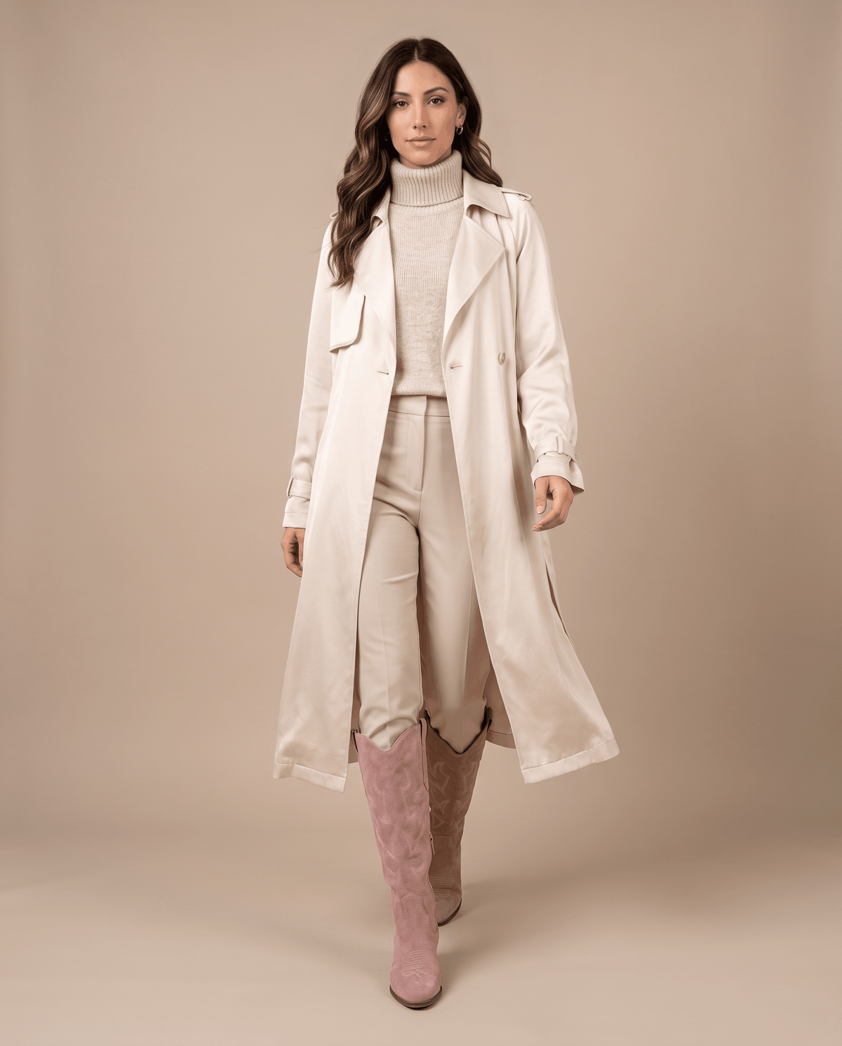 Woman in a long cream trench coat and trousers walking in pink western boots