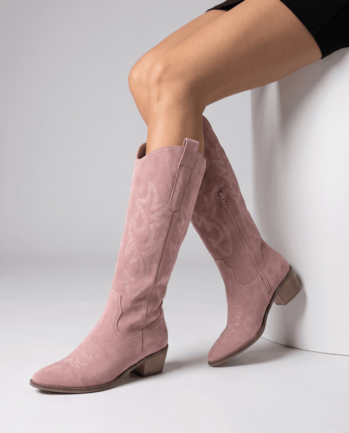 Seated model with bare legs crossed wearing pink embroidered western boots
