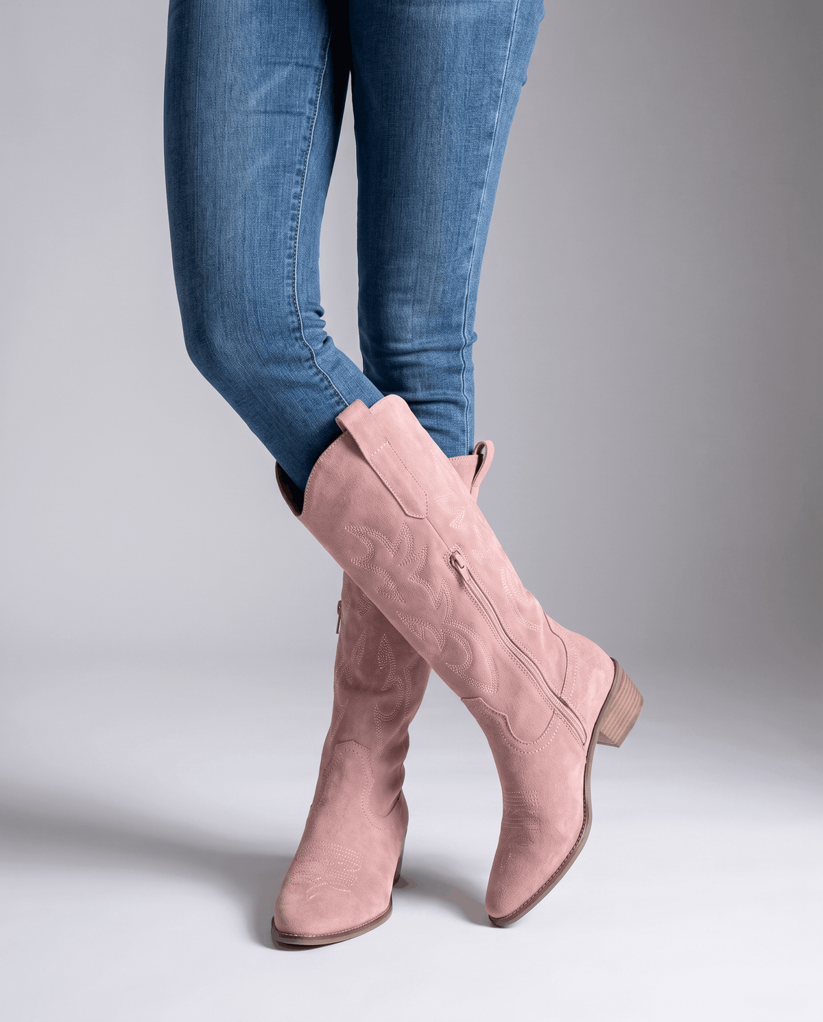 Pink tall boots worn standing with blue skinny jeans tucked inside