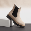 Beige suede Chelsea ankle boot with black elastic panels and lug sole displayed on a white pedestal.