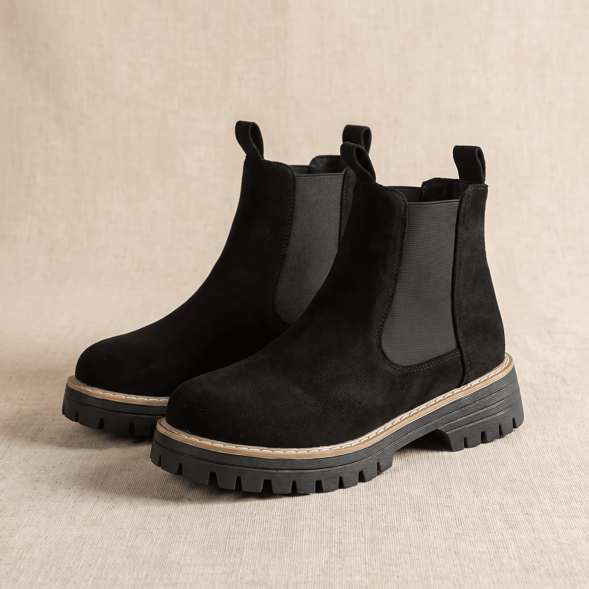 Pair of black suede Chelsea ankle boots with lug soles on a neutral background.