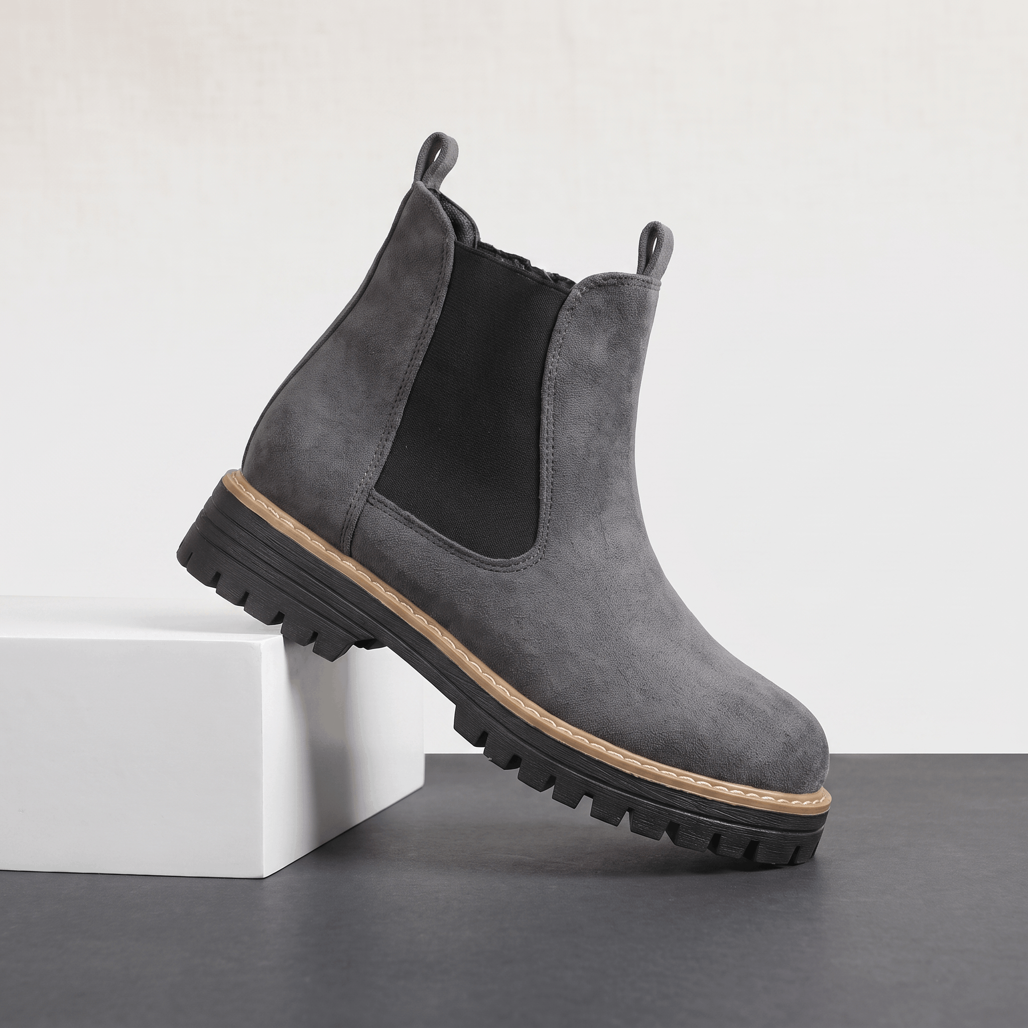 Gray suede Chelsea ankle boot with a lug sole displayed on a white pedestal.