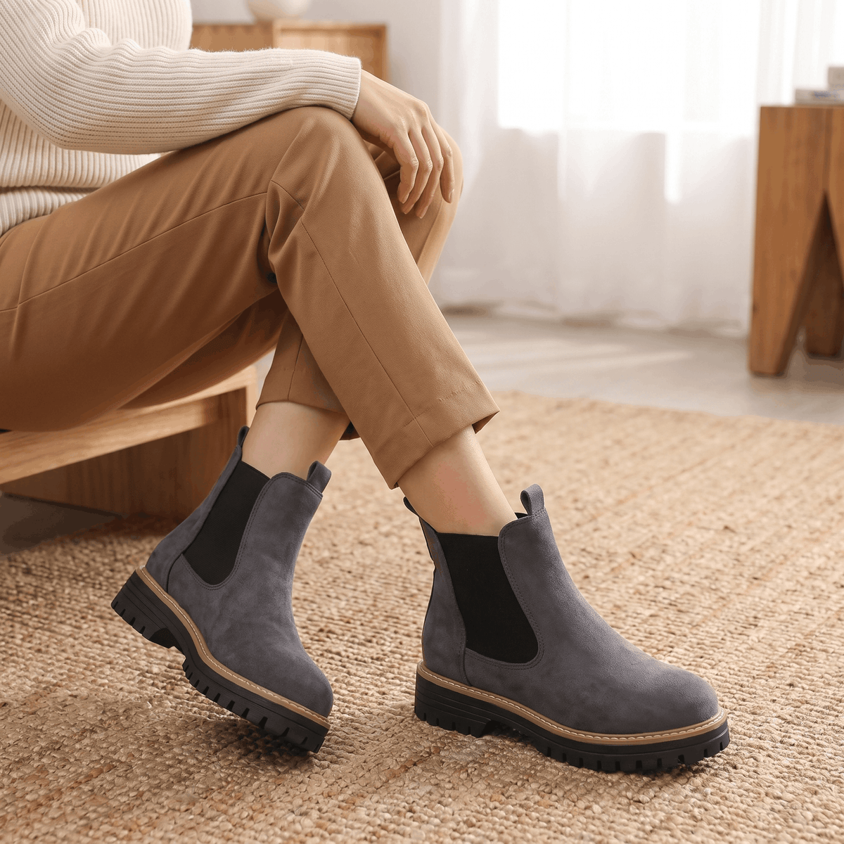 Woman seated wearing gray suede Chelsea ankle boots with beige trousers.