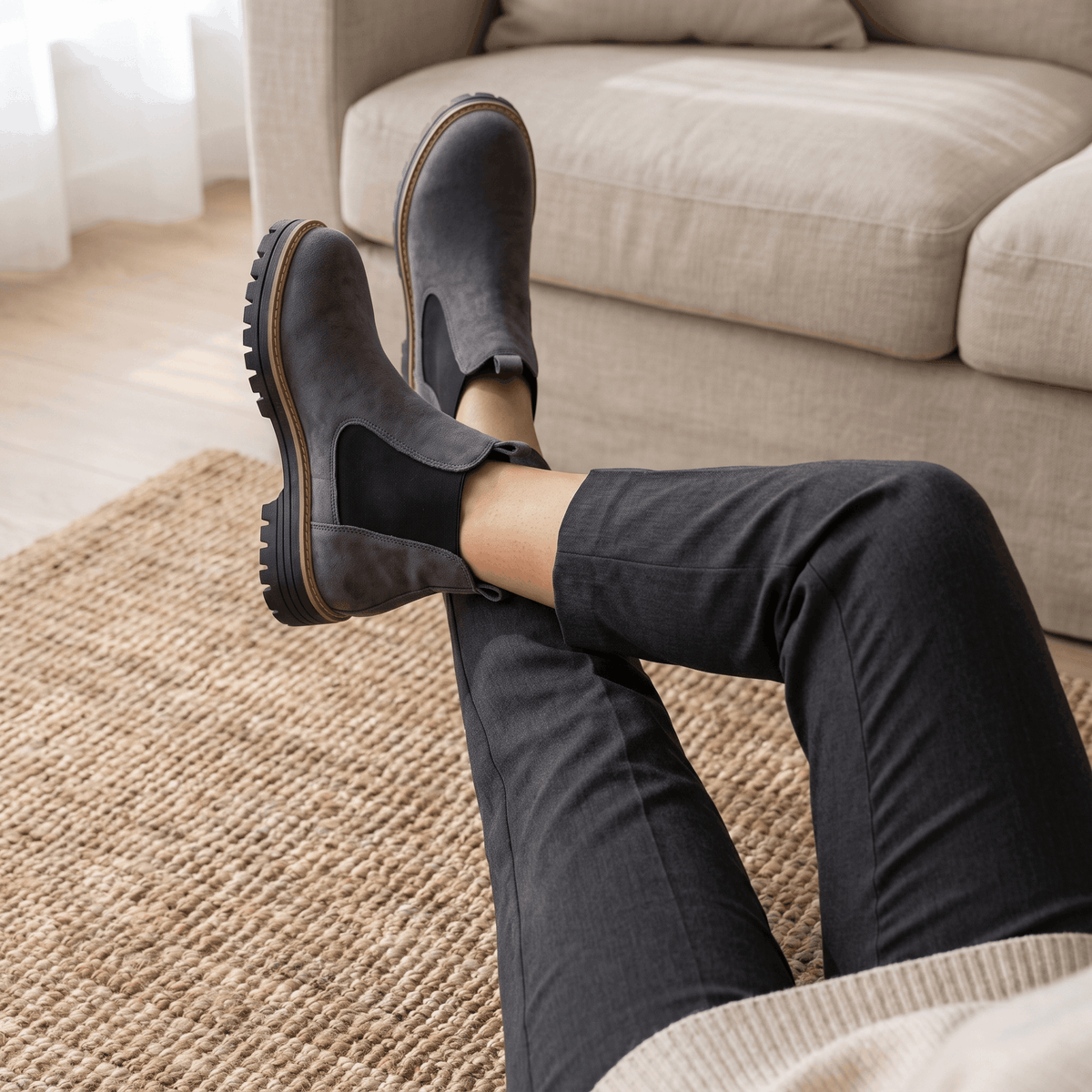 Woman standing indoors holding gray suede Chelsea ankle boots.