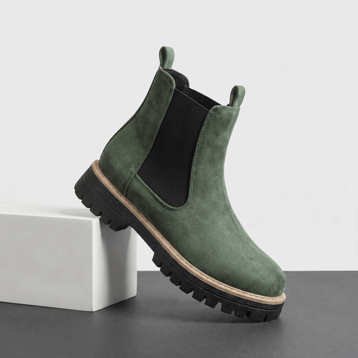 Green suede Chelsea ankle boot with a lug sole displayed on a white pedestal.