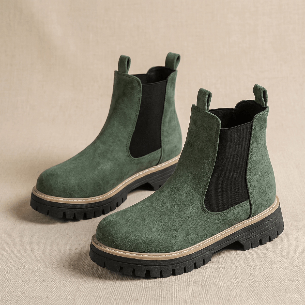 Pair of green suede Chelsea ankle boots with lug soles on a neutral background.