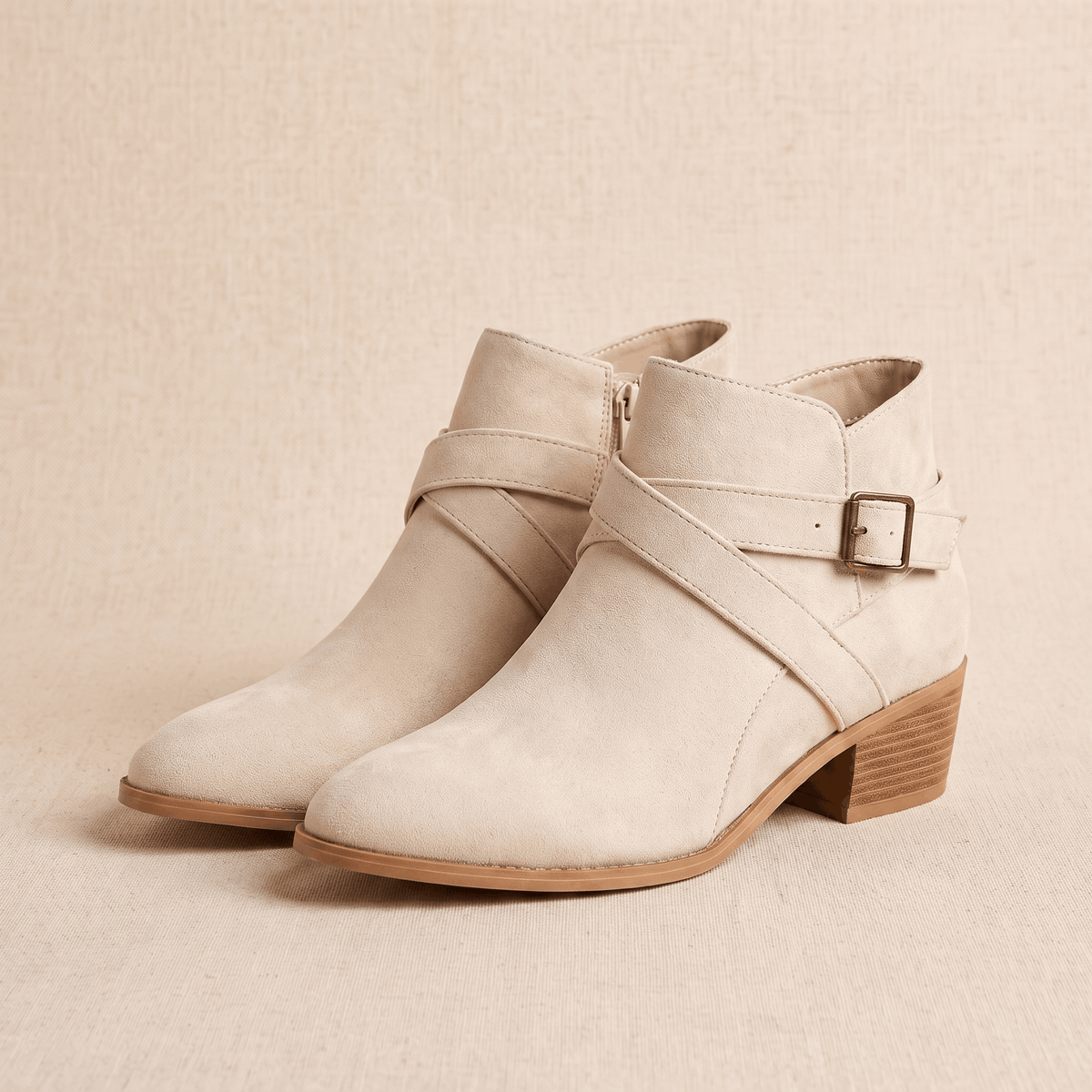Pair of beige suede ankle boots with wraparound straps and buckle details on a neutral background.