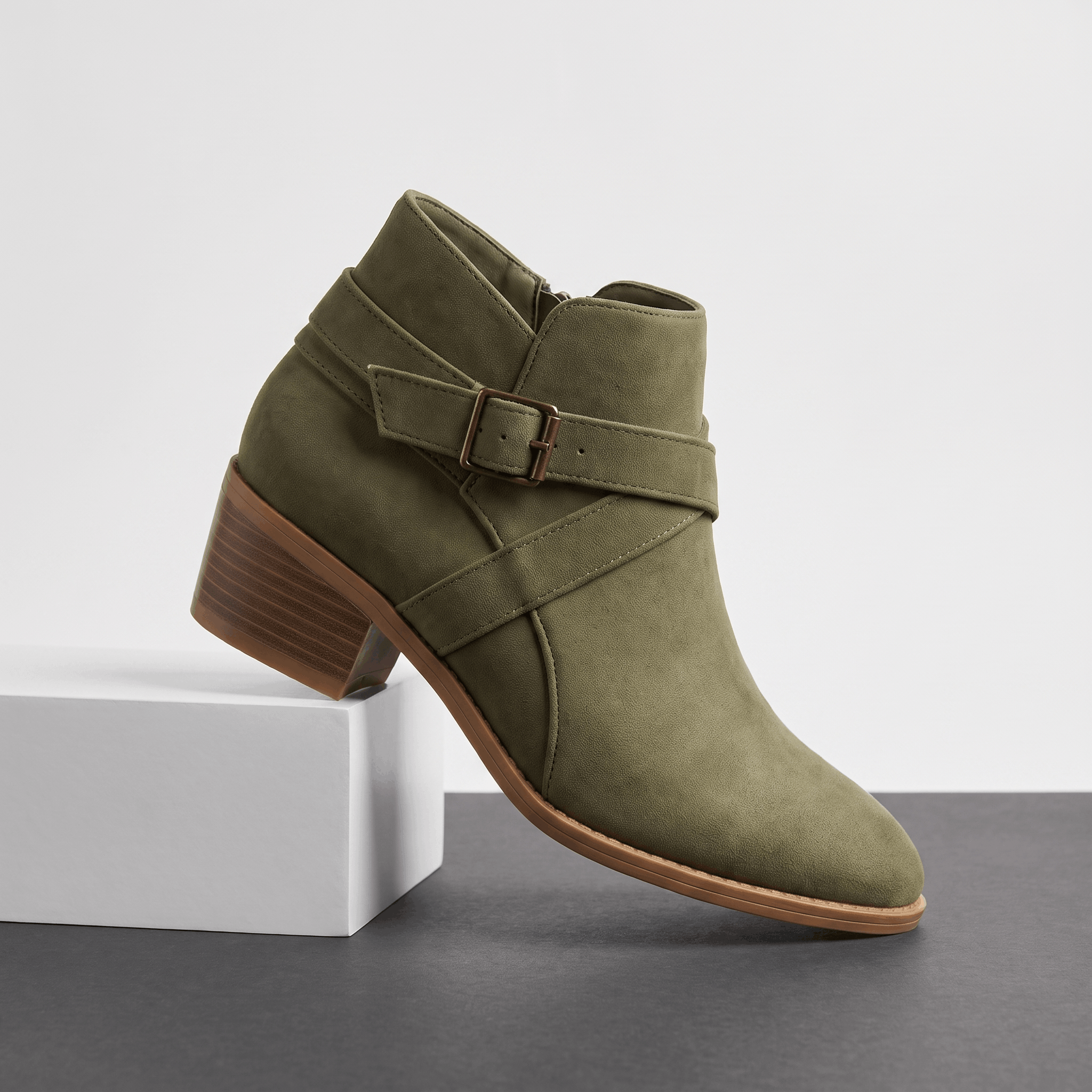 Green suede ankle boot with wraparound straps and a block heel displayed on a white pedestal.