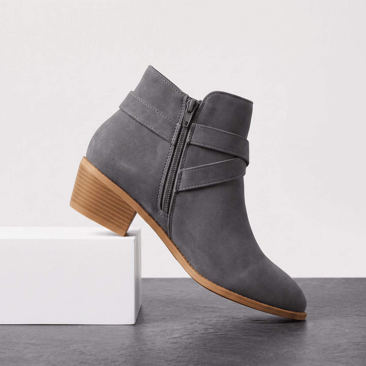 Gray suede ankle boot with wraparound straps and a block heel displayed on a white pedestal.