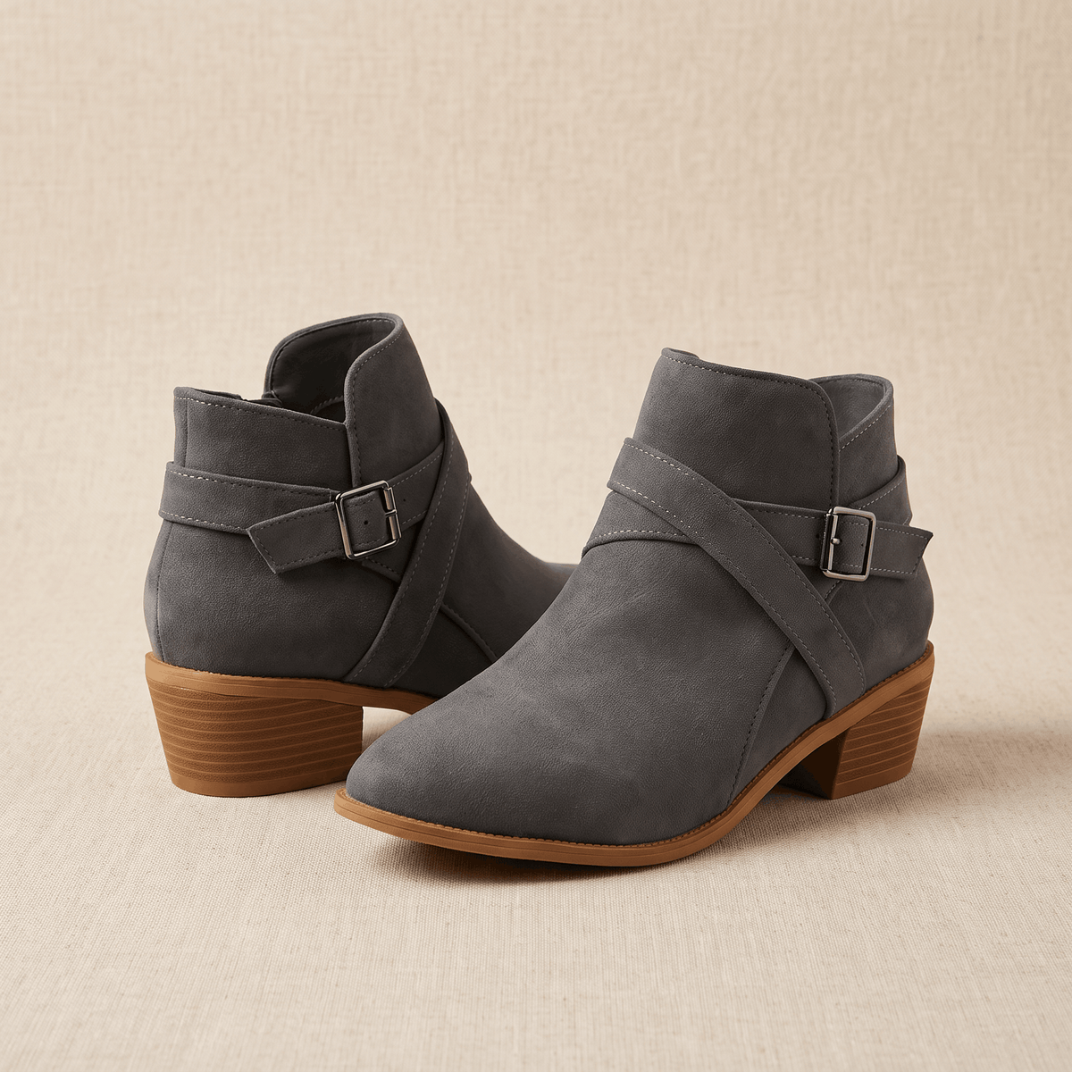 Pair of gray suede ankle boots with buckle details on a neutral background.
