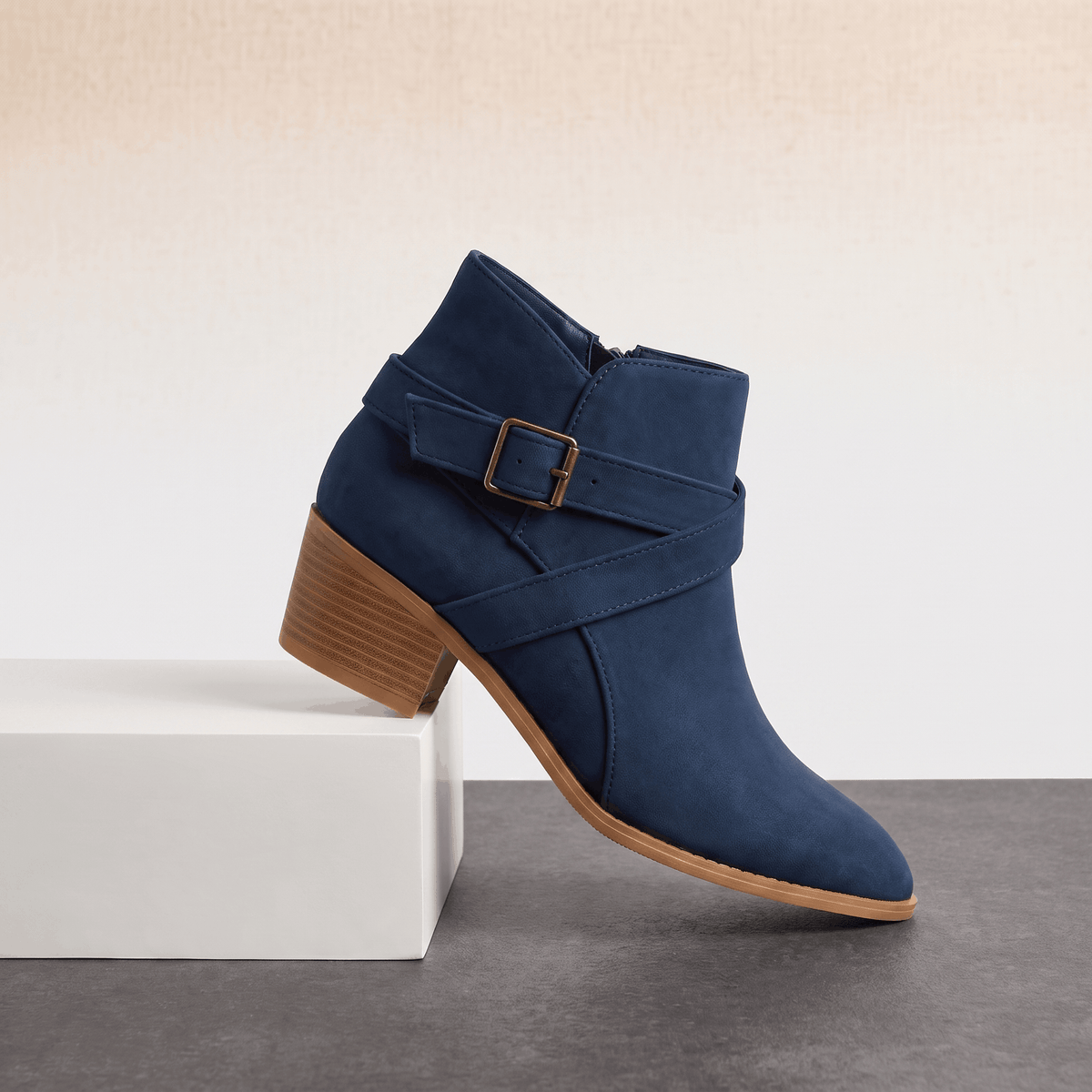 Blue suede ankle boot with wraparound straps and a block heel displayed on a white pedestal.