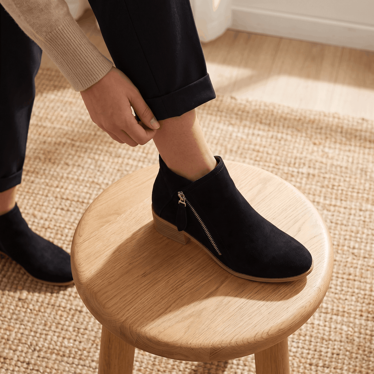 Close-up of a person wearing black suede ankle boots indoors.