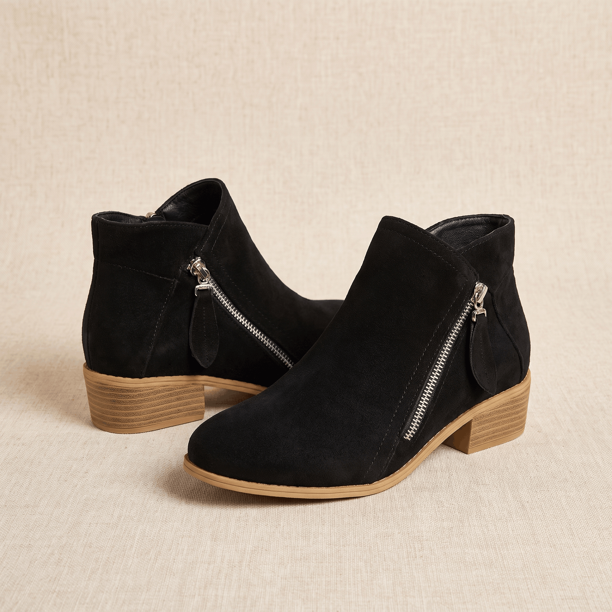 Pair of black suede ankle boots with side zippers on a neutral background.