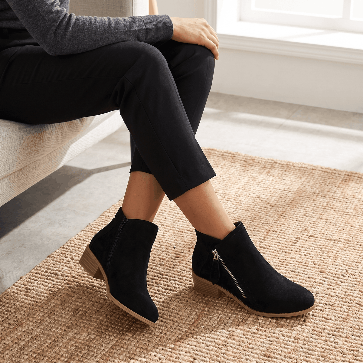 Woman wearing black suede ankle boots with dark trousers.