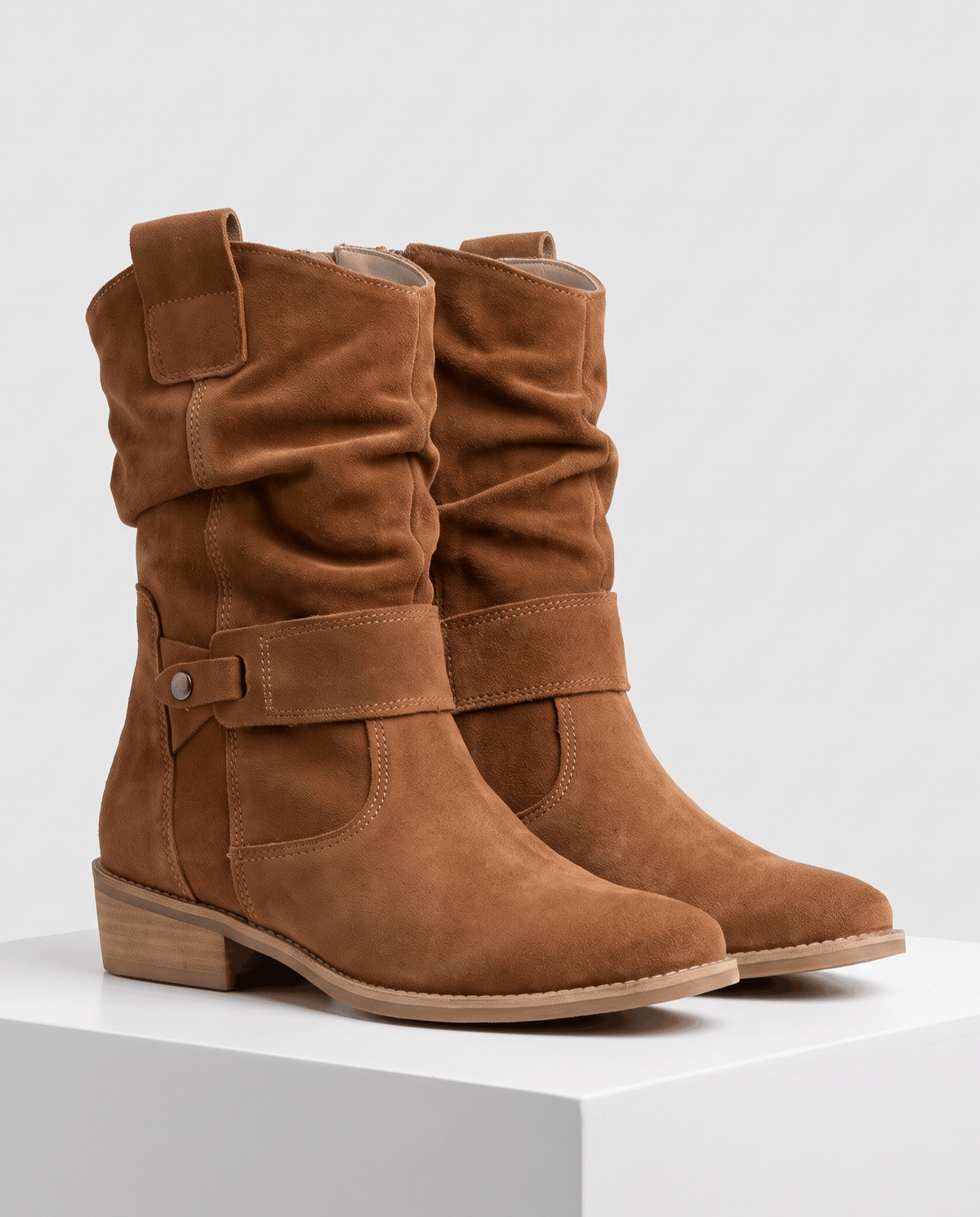 Pair of tan suede slouch boots on a white pedestal