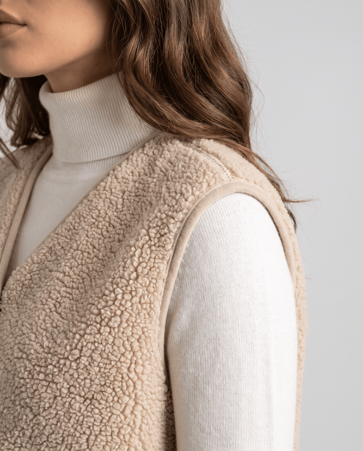 Side close-up of beige teddy fleece vest showing the soft texture over a white turtleneck