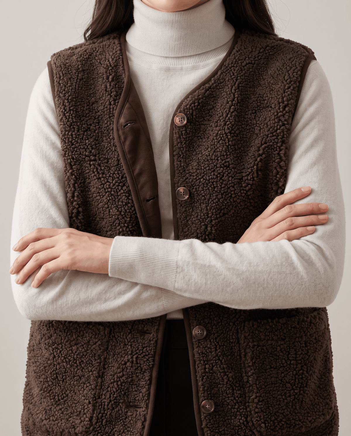 Close-up of brown teddy fleece vest with arms crossed, showing buttons and patch pocket
