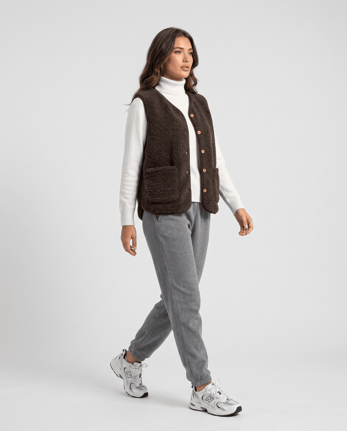 Woman walking in brown teddy fleece vest over a white turtleneck with gray joggers and sneakers