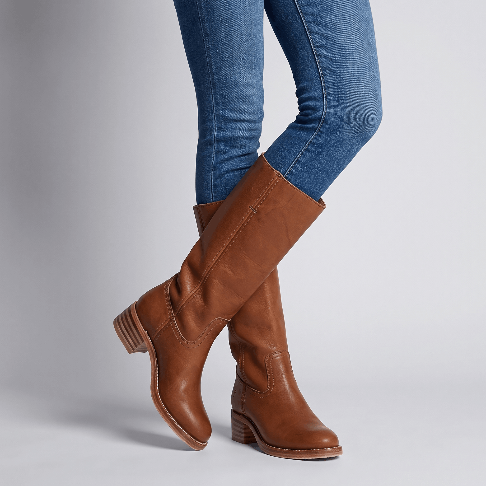 Woman wearing dark brown vegan leather knee-high riding boots with blue jeans.