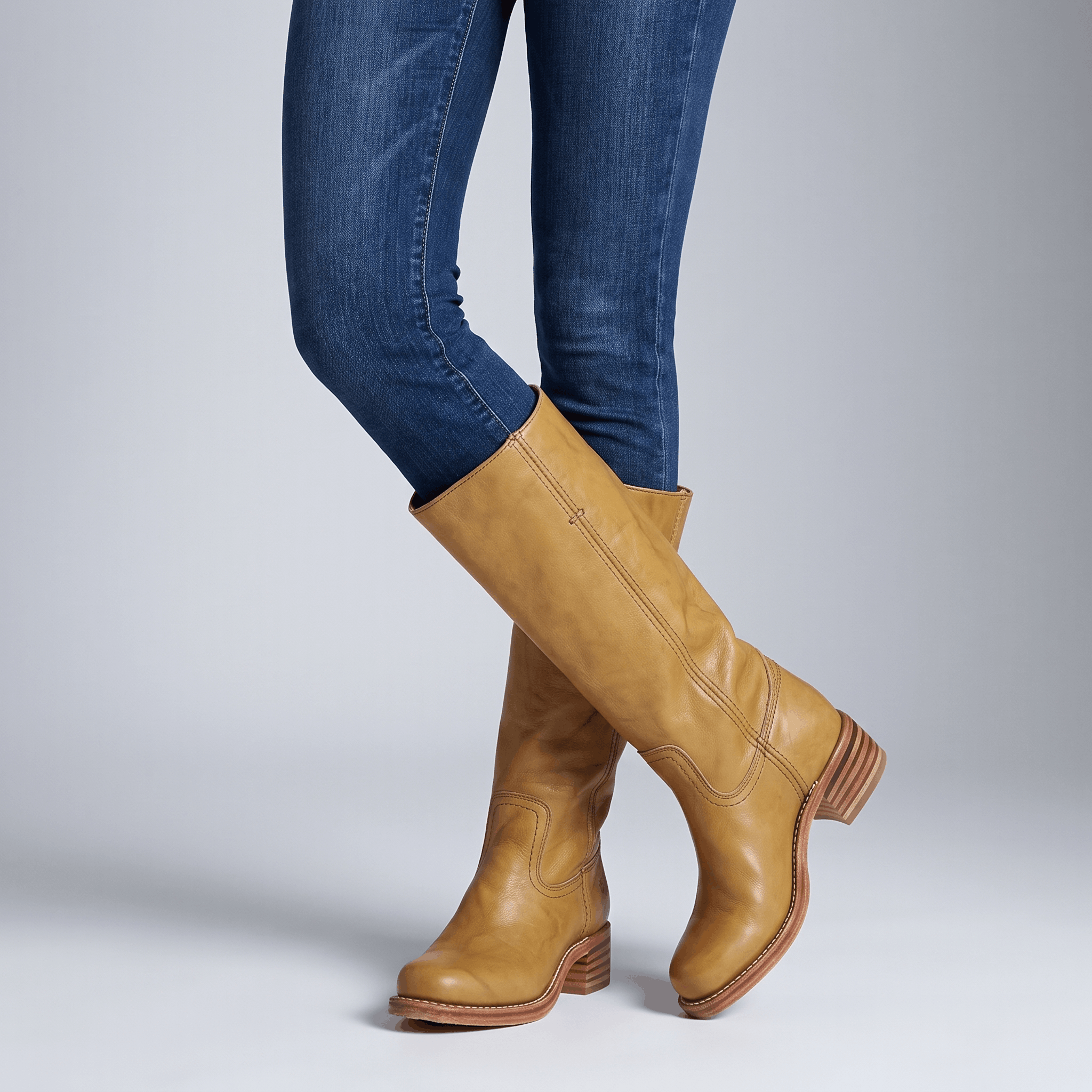 Woman wearing tan vegan leather knee-high boots with blue jeans.