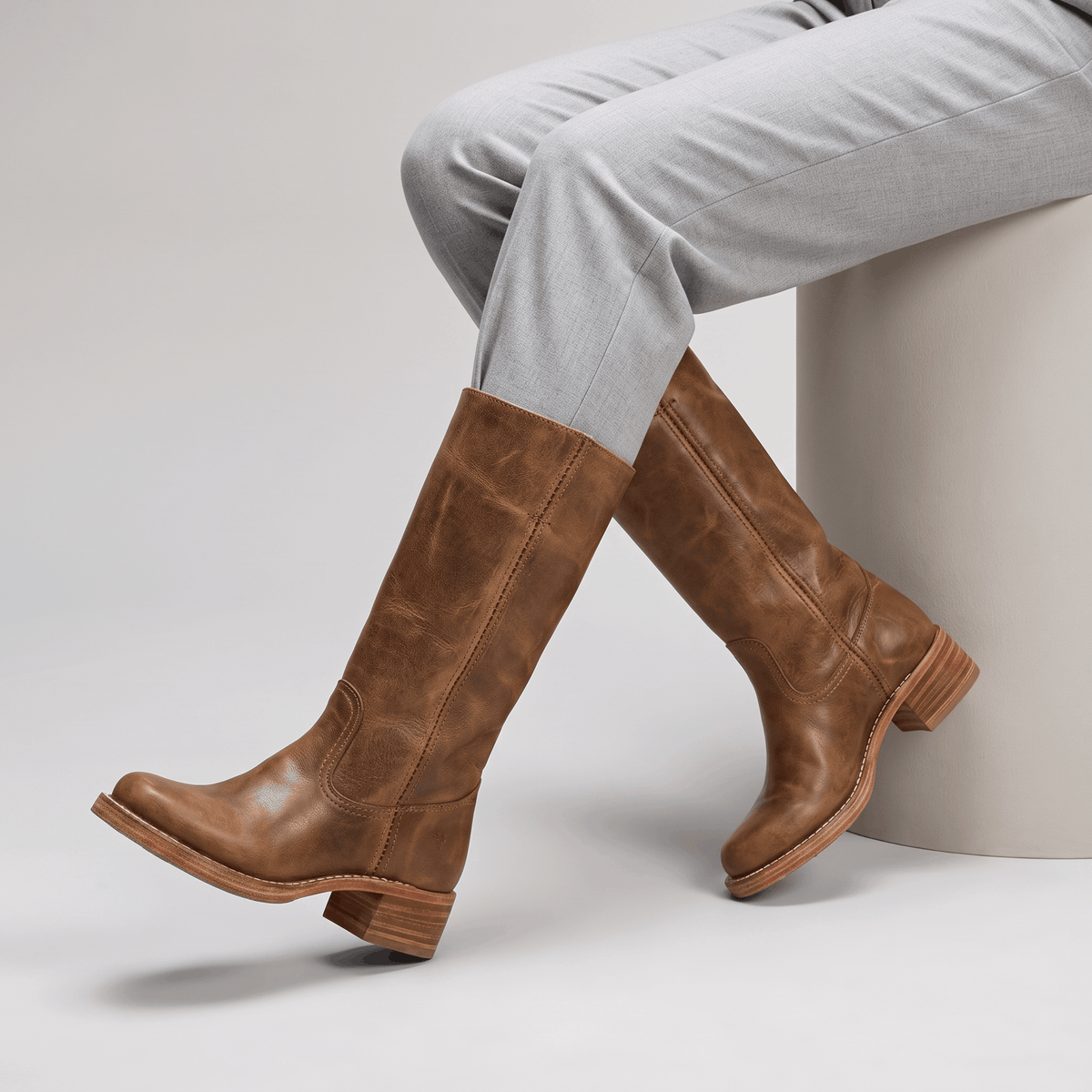 Woman wearing brown vegan leather knee-high boots with light-colored trousers.
